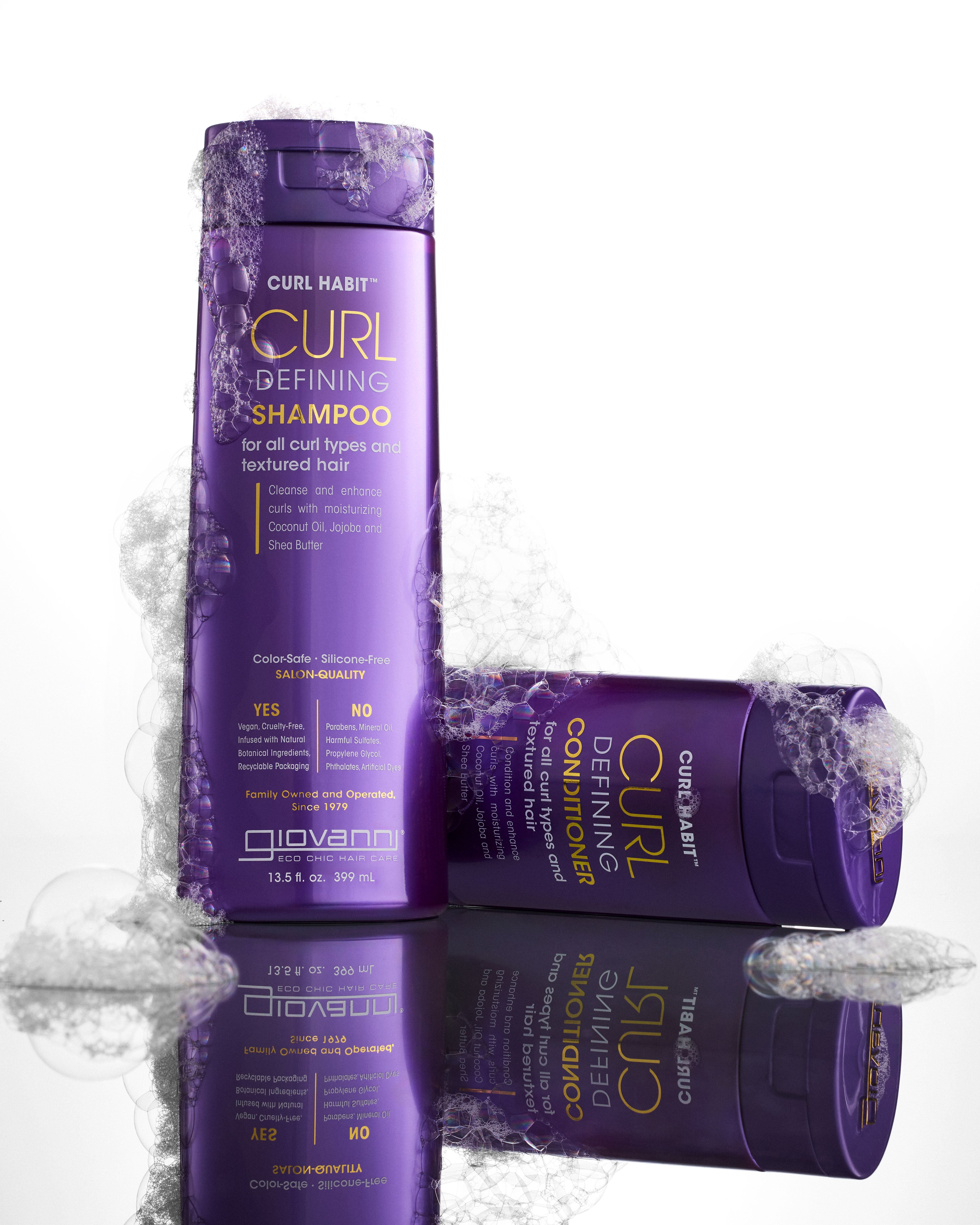 Two purple bottles of Giovanni Cosmetics CURL HABIT™ Curl Defining Shampoo, in two sizes and infused with moisturizing oils for curls, rest on a white background with playful bubbles—one upright, one lying on its side.