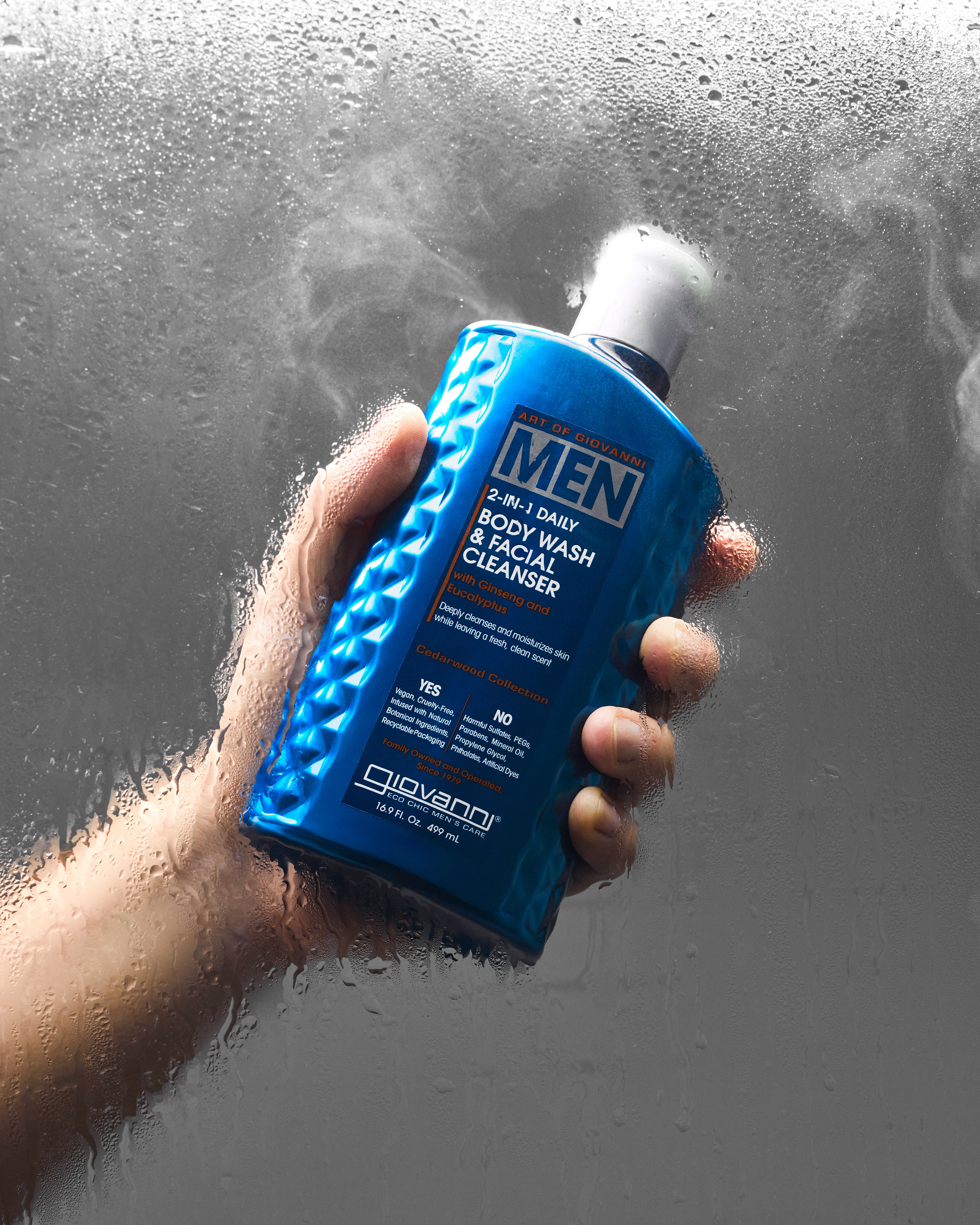 Hand holding a blue bottle of Giovanni Men's body wash against a gray background