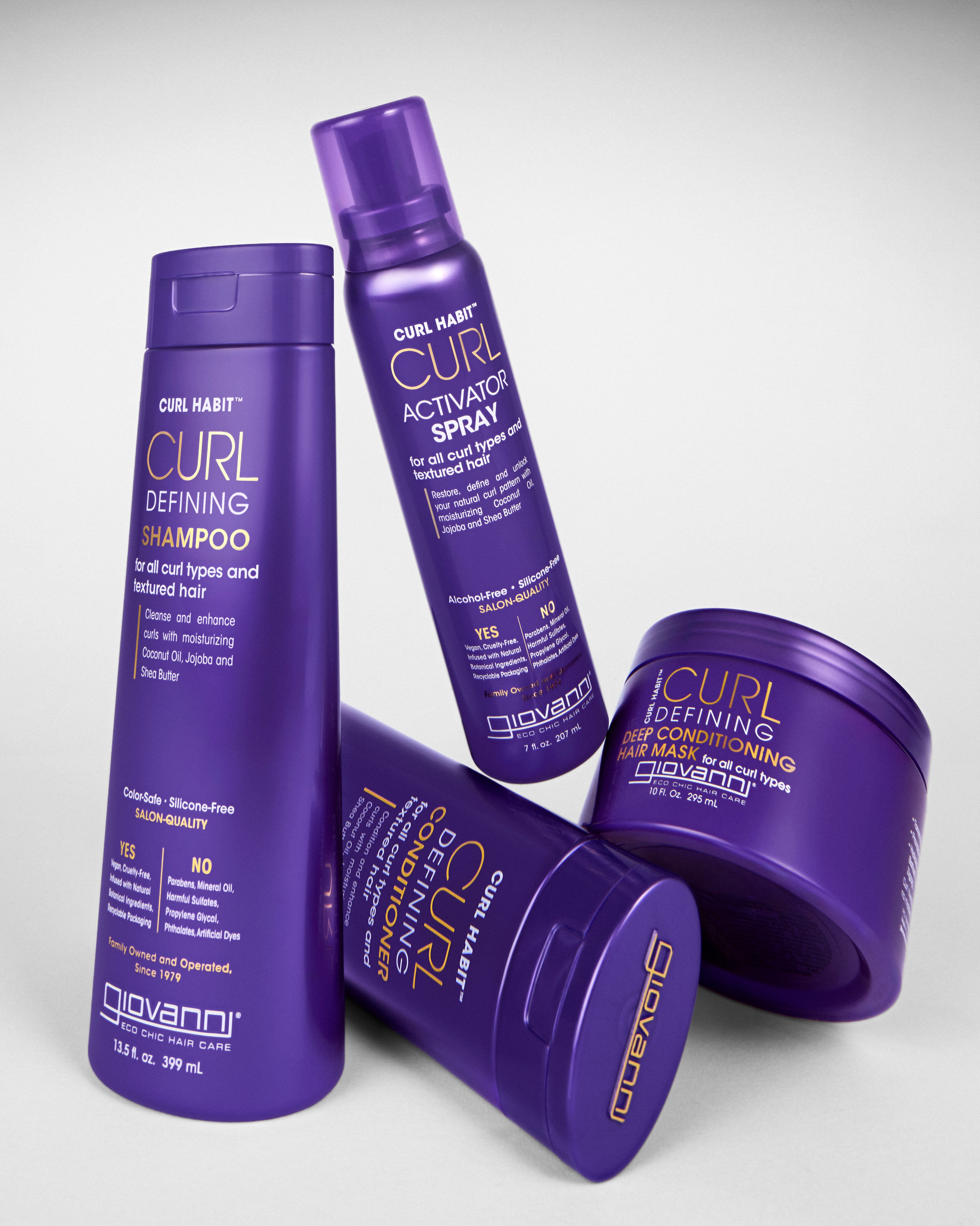 Four Giovanni Cosmetics CURL HABIT™ Curl Defining Shampoos in purple bottles, designed to moisturize and define curls, are arranged on a white surface.