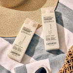 Two bottles of Giovanni Cosmetics DIRECT LEAVE-IN™ WEIGHTLESS MOISTURE CONDITIONER sit on a striped towel beside a sun hat, white sunglasses, and bag, highlighting weightless moisture in a relaxed, summery scene.