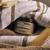 Image of Smoothing Castor Oil Strengthening Hair Mask snuggled in bath towels. 