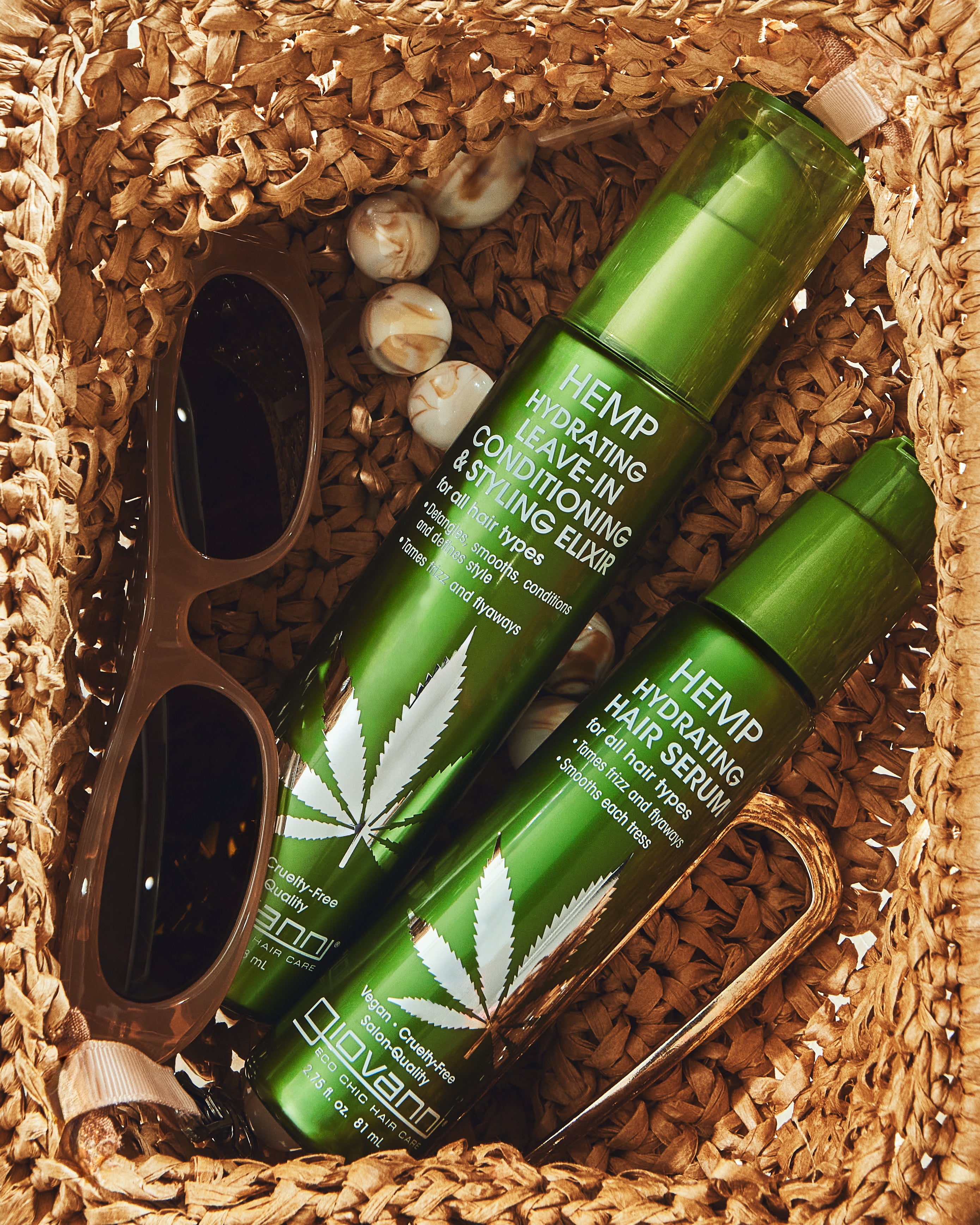 Hemp Hydrating Leave-In Conditioning & Styling Elixir and Hair Serum bottles nestled in raffia basket with sunglasses and gold hair clip.