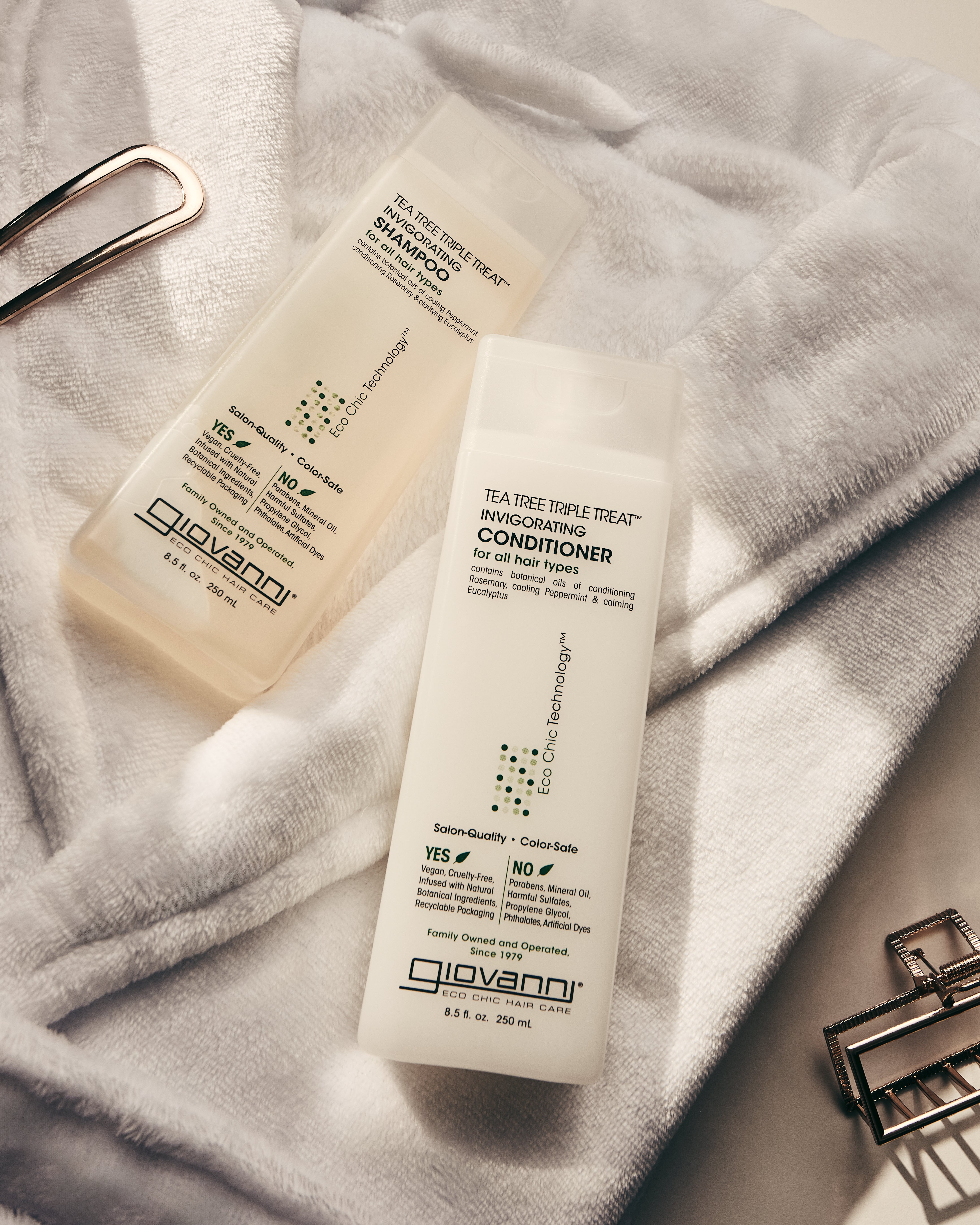Bottles of Tea Tree Triple Treat Shampoo and Conditioner laying on crisp white bath robe.