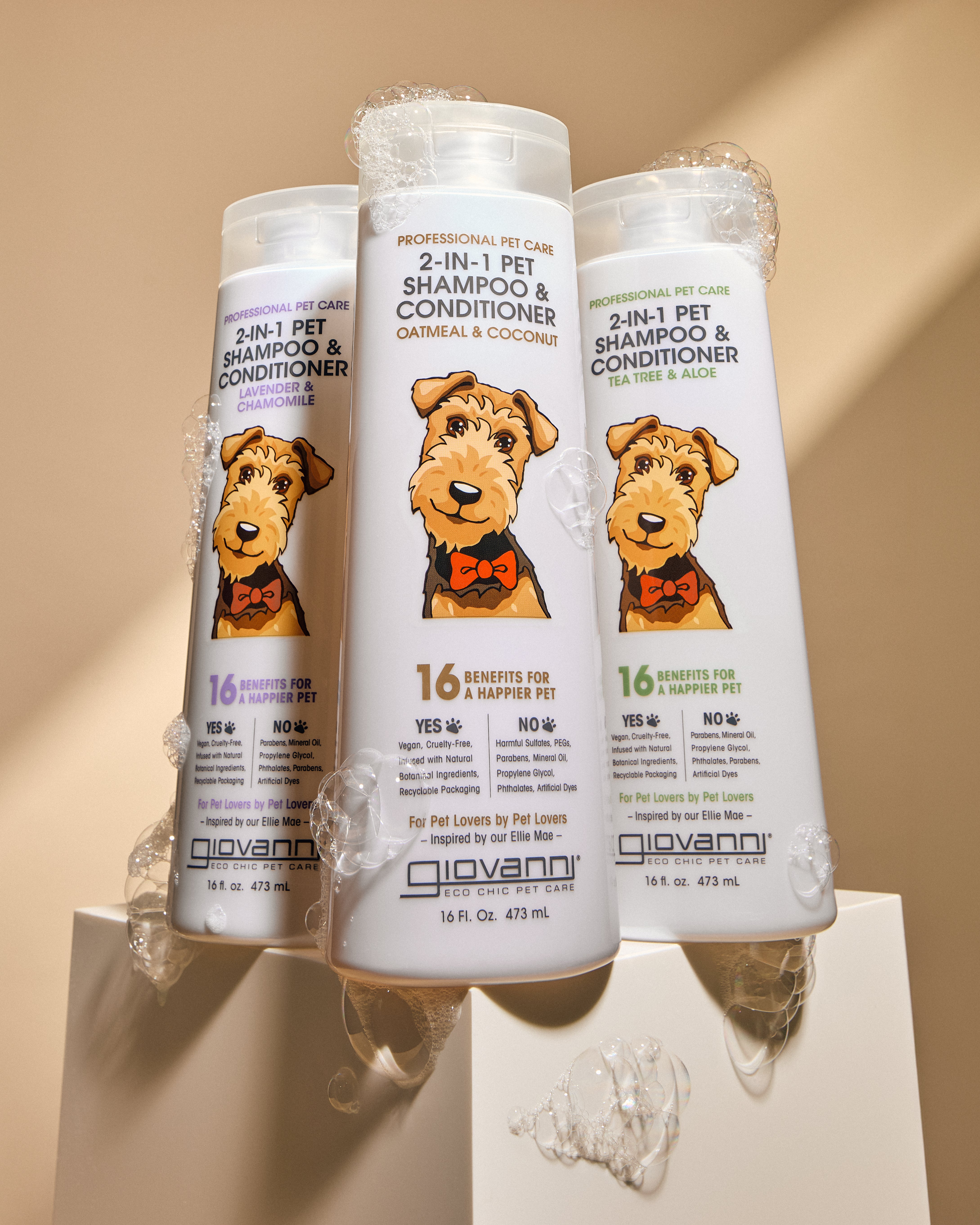Three white bottles of Giovanni 2-in-1 Pet Shampoo & Conditioner arranged on a pedestal with gel, shown against a warm beige background.