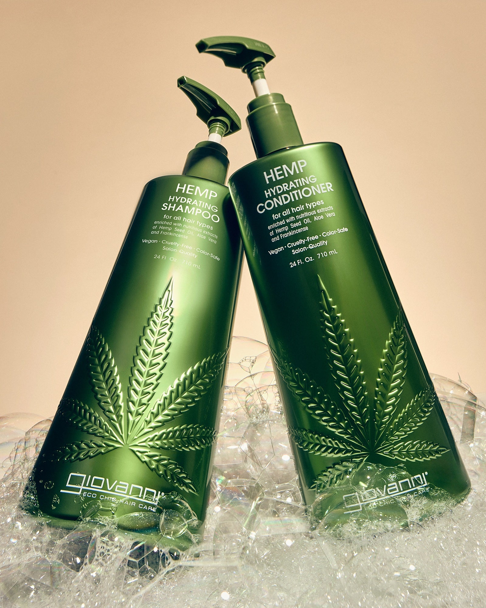 Two bottles of Giovanni Hemp Hydrating Hair Care products, including shampoo and conditioner, standing in a fluffy pile of bubbles against a warm beige background.