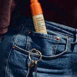 A bottle of ULTRA VOLUME Super Potion Hair Volumizing Styling Booster tucked into the pocket of blue jeans next to keys.