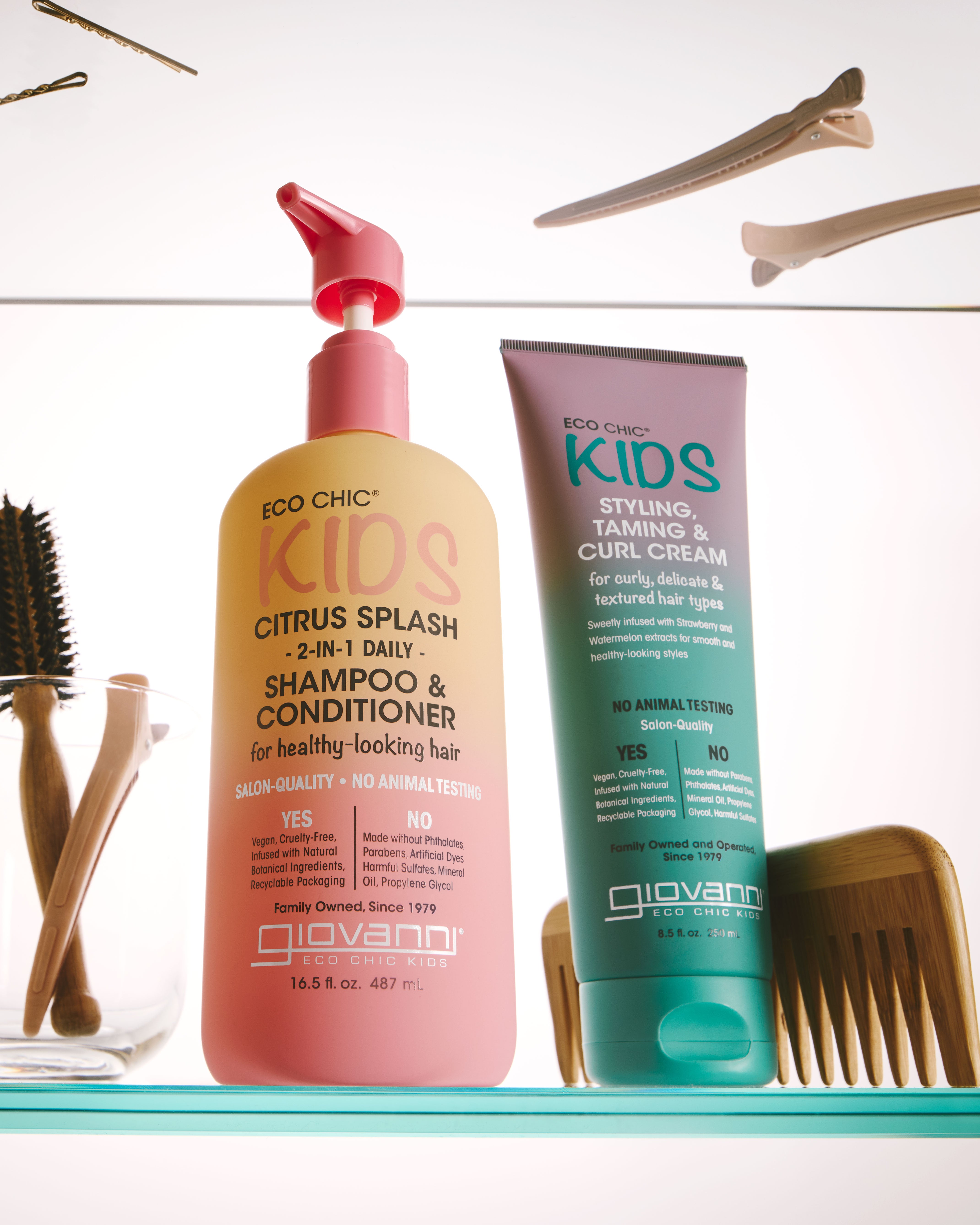 Image of two products - Giovanni's Citrus Splash 2-in-1 Shampoo and Conditioner and KIDS Styling, Taming & Curl Cream on a glass shelf in a bathroom setting. 
