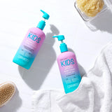 Two bottles from the Giovanni Cosmetics KIDs Bundle are arranged on a white surface beside a fluffy white towel, a yellow sponge, and a wooden brush. The bundle includes their gentle 2-in-1 shampoo and conditioner along with a nourishing body wash—an ideal combination for caring for your child’s delicate hair and skin.