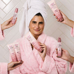 Woman in a pink robe holding a bottle of 
Giovanni 2Chic Frizz Be Gone Shampoo surrounded by hands holding other Frizz Be Gone products