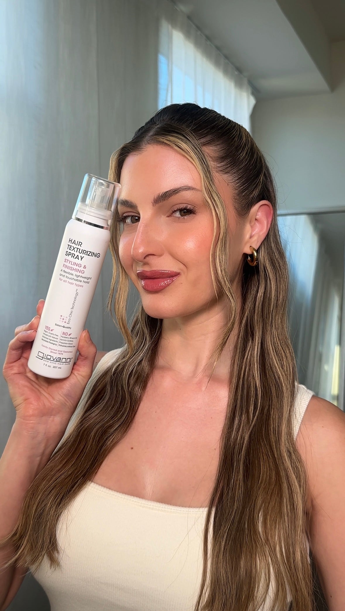 Woman holding a hair texturizing spray bottle in front of a mirror