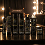 Bottles of Giovanni Professional Collection products on a dark reflective surface, including shampoo, conditioners, hair serum, hair styling gel, and pomade, with warm blurred lights in the background.